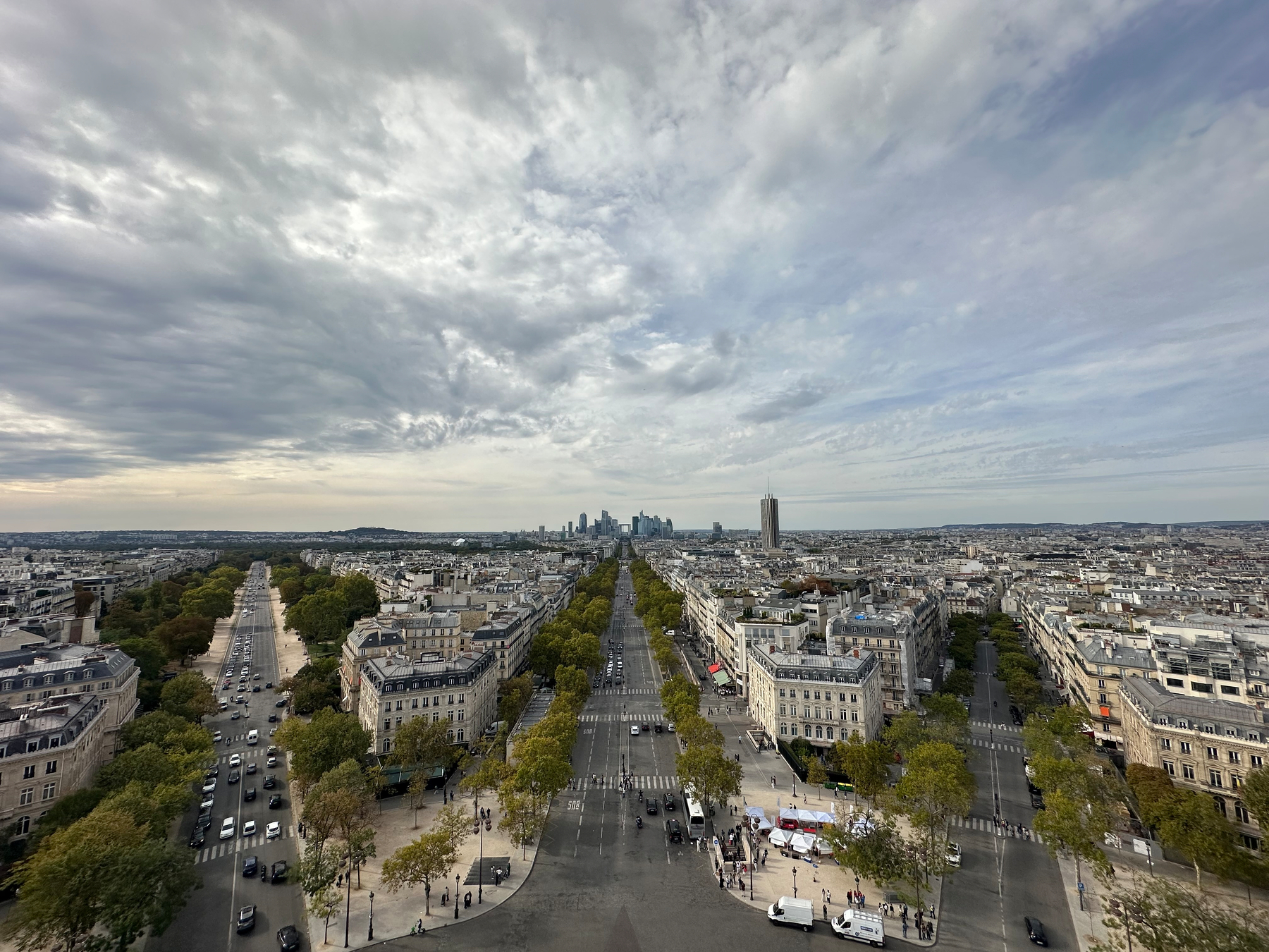 A wide, elevated view of a cityscape with tree-lined streets converging toward a modern skyline under a cloudy sky.