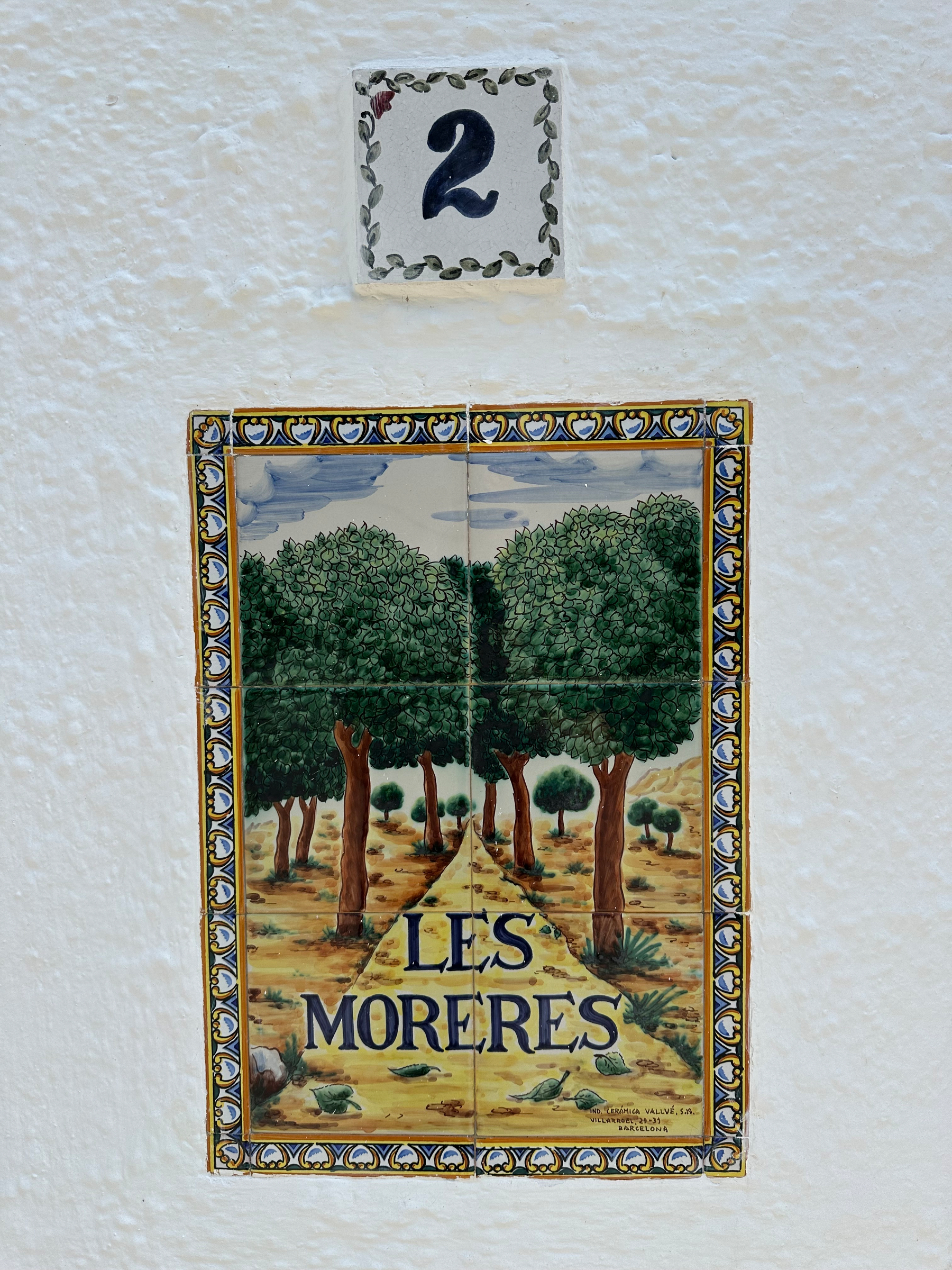 The wall features a decorative tile with the words LES MORERES below a scenic illustration of trees, and above it is a tile displaying the number 2.