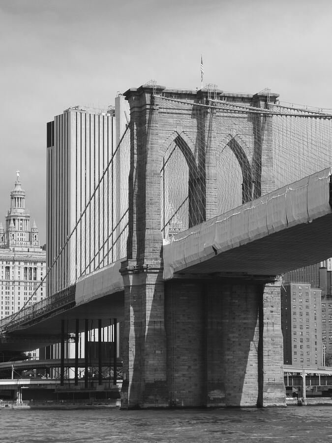 A black and white photograph of the Brooklyn Bridge with city buildings in the background.